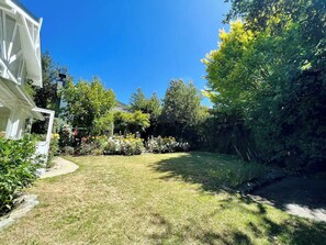 Ein gepflegter Garten mit verschiedenen Pflanzen und Blumen, ein klarer Himmel und ein Weg, der zu einem Gebäude führt.