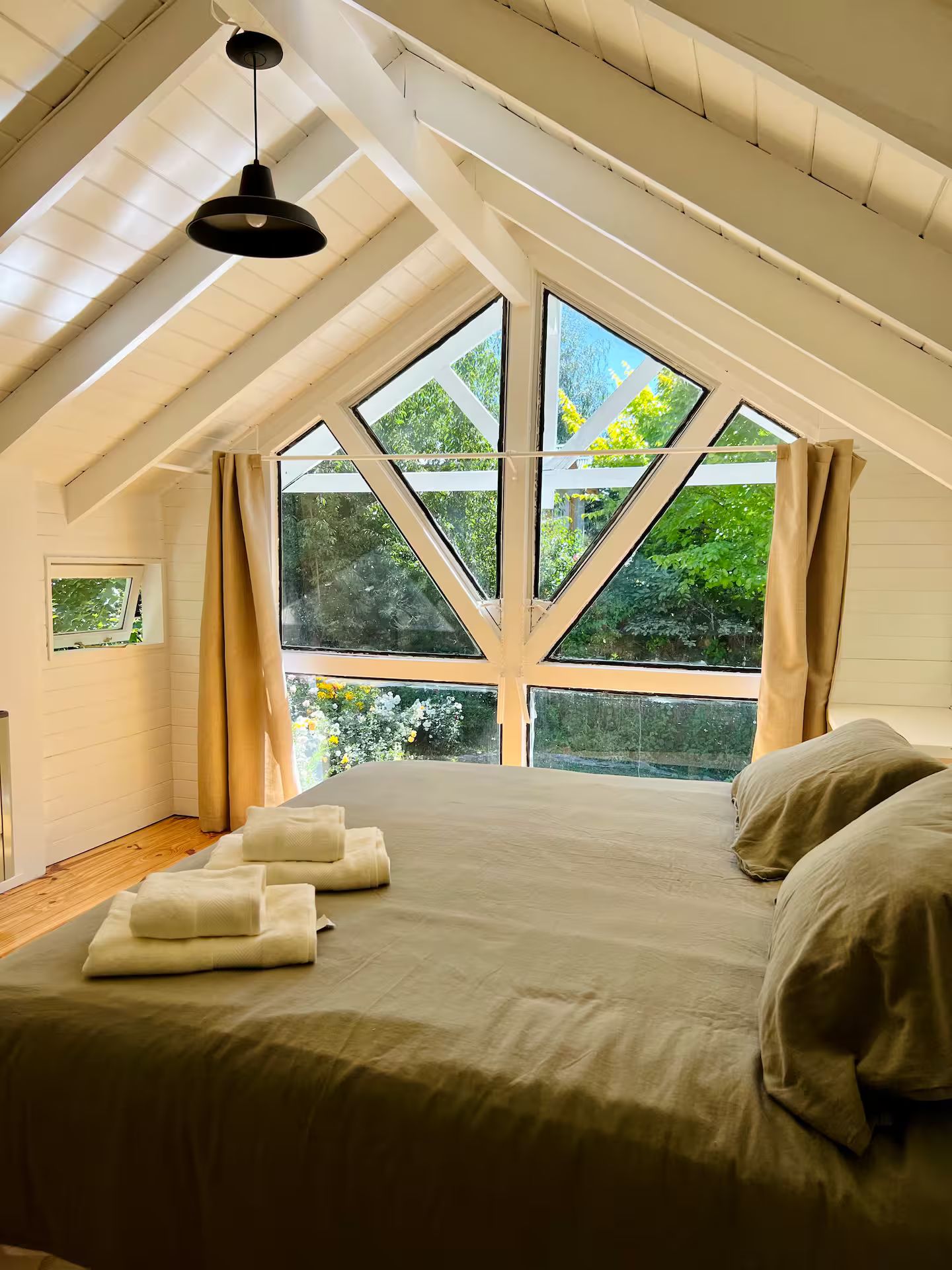 Un dormitorio con techo inclinado, ventanas amplias y una cama con almohadas y toallas.