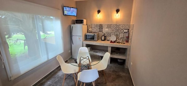 A compact kitchen with a dining table and chairs, a microwave, a refrigerator, and a television mounted on the wall.
