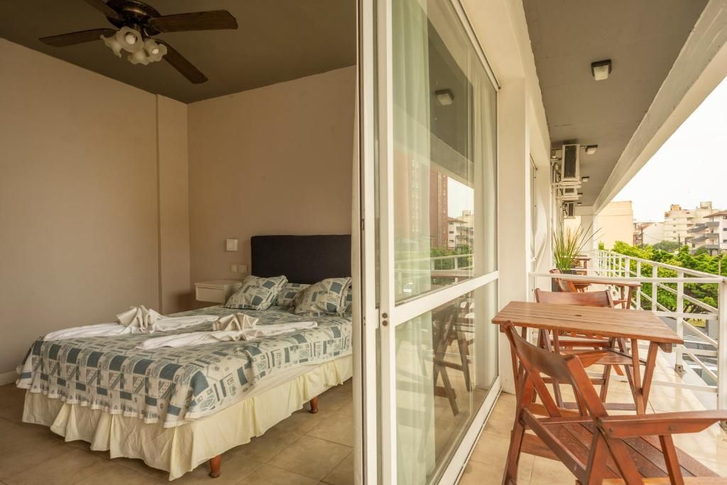 A bedroom with a bed, a ceiling fan, and a balcony with a table and chairs.