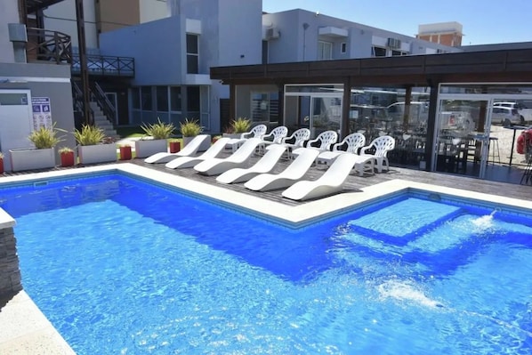 Piscina con sillones de descanso y una zona de estar techada.