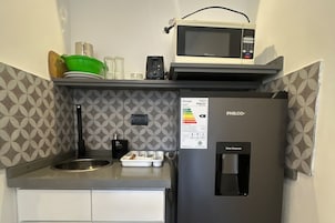Una kitchenette compacta con un refrigerador PHILCO, un microondas, un dispensador de agua y un lavamanos.