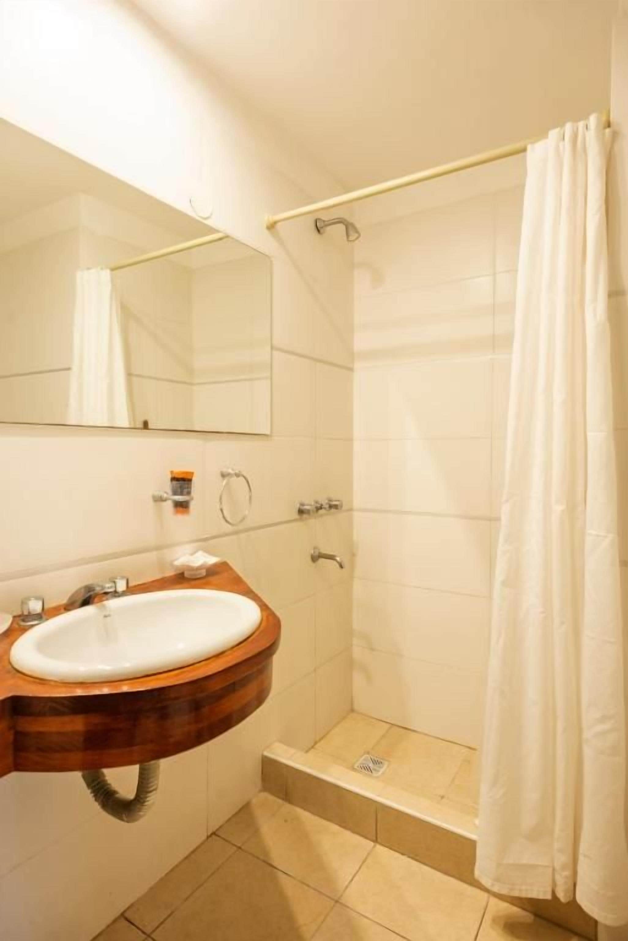 Een badkamer met een houten wastafelmeubel, een spiegel, een witte wasbak en een douche met een wit gordijn.