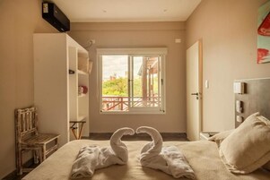 Una habitación de hotel con cama, un banco, una ventana con vistas y una puerta.