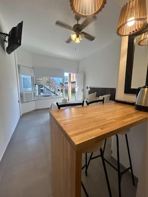 A modern kitchen with a wooden countertop, bar stools, a ceiling fan, and a large window offering a view of a staircase. - Hotel Marítimo (Villa Gesell)
