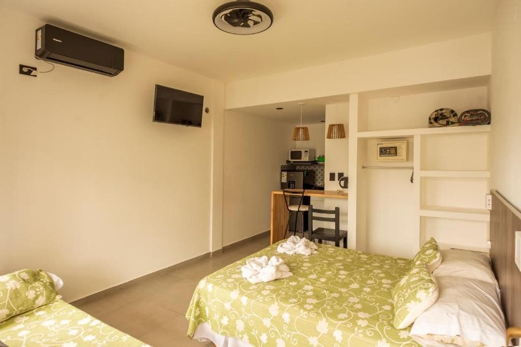 Une chambre d’hôtel comprenant un lit, un bureau avec une chaise, un téléviseur fixé au mur et une étagère avec divers objets.