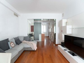 Ein modernes Wohnzimmer mit einer Eckcouch, einem Flachbildfernseher und Holzboden.