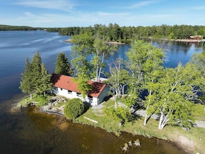 A lakeside property with a single-story house, a dock, and a forested shoreline.
