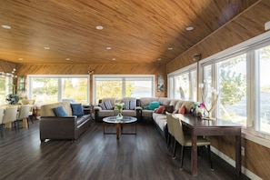 A spacious living room with a wooden ceiling, large windows, and a view of the outdoors.