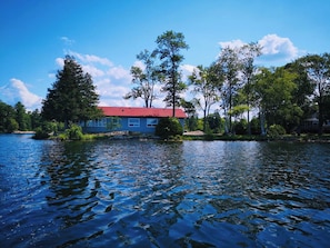 A house with a red roof by a calm lake, surrounded by trees.