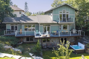 A two-story house with a deck, outdoor seating, and a hot tub. - Luxury Whitefish Retreat-Hot Tub, Fire Pit, Sauna, Waterfall (Whitefish)