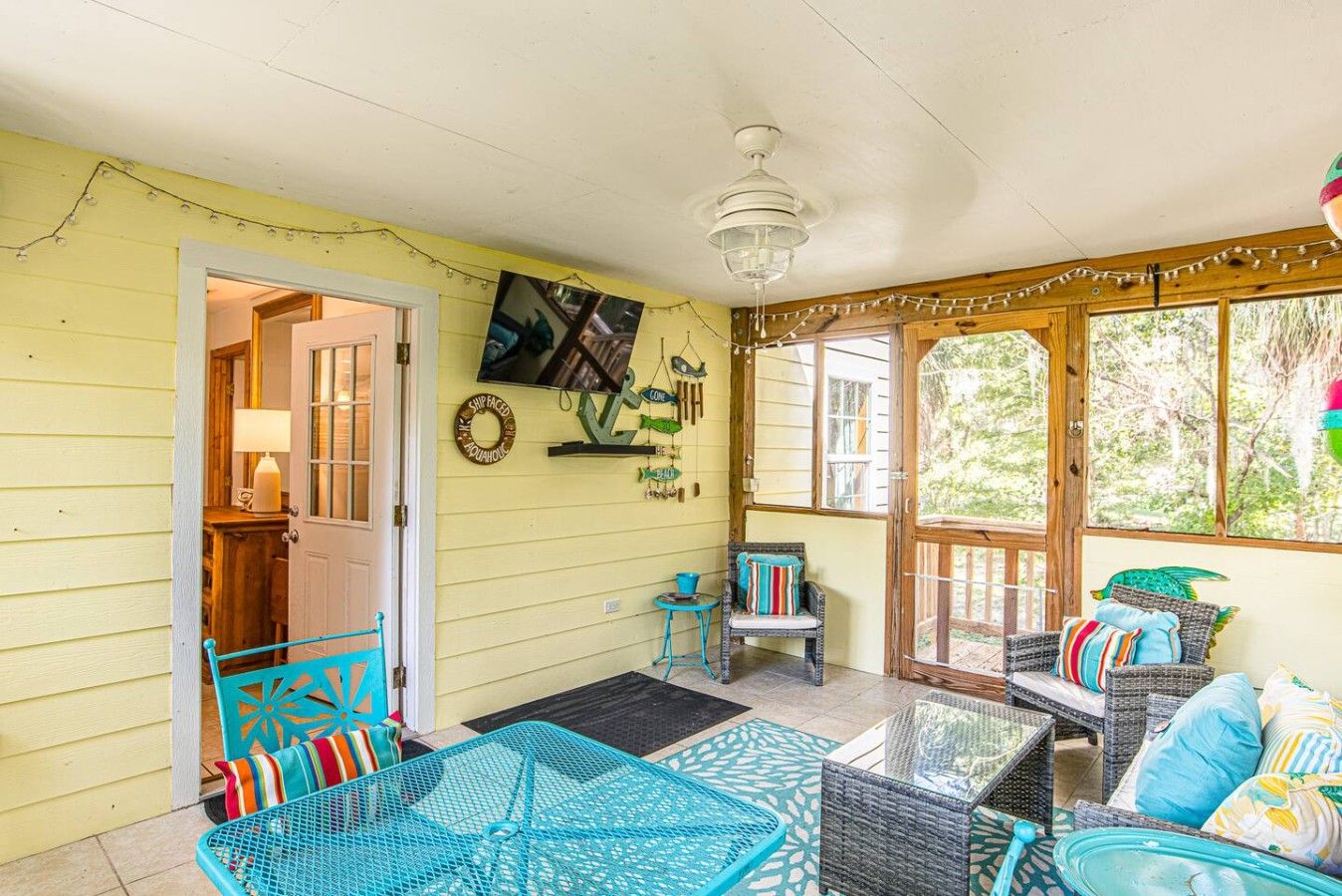 A covered porch with wicker furniture, a television mounted on the wall, and a door leading to an interior room.