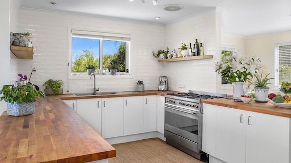 Une cuisine moderne avec des meubles blancs, un plan de travail en bois, une cuisinière à gaz et divers appareils de cuisine.