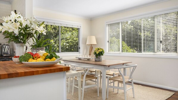 A bright kitchen with white cabinetry, a wooden countertop, a dining table with chairs, and a view through large windows. - Rockys Beach House Beachfront Escape with Sweeping Ocean Views (Manyana)