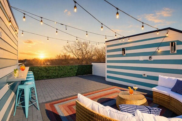 An outdoor patio with string lights, a table with drinks, and a seating area with cushions. - Game-day escape: 3 rooftop homes sleep 36 near Geodis Park, Nashville (Nashville)