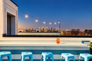 A rooftop bar with a city skyline view, string lights, and blue bar stools. - 2 Nashville homes, rooftop + fire pit, sleeps 24 near Geodis Park (Nashville)