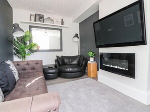 Ein Wohnzimmer mit einem braunen Sofa, einem schwarzen Ledersessel, einem weißen Kamin und einem flachbildfernseher an der Wand.