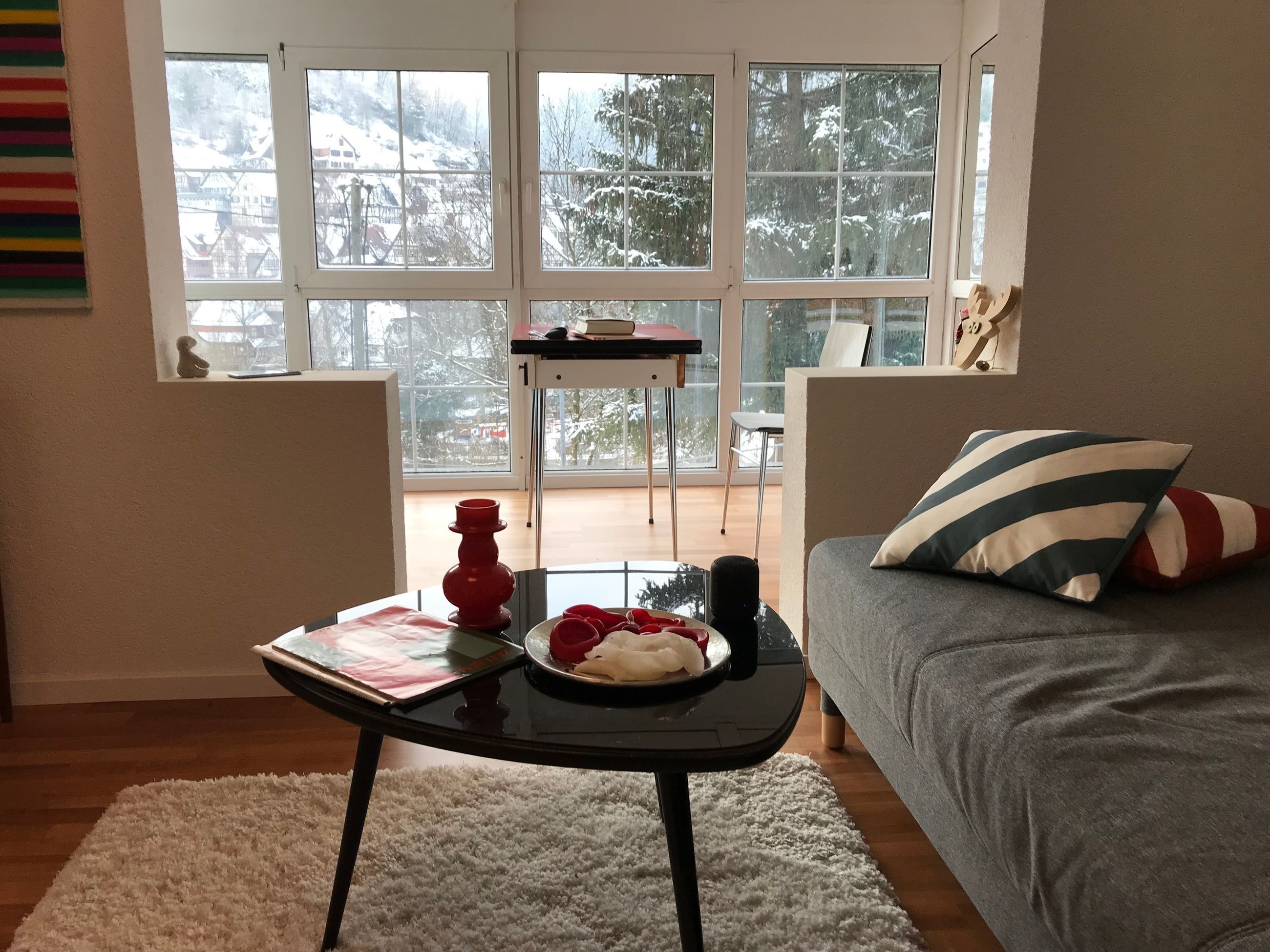 Una sala de estar acogedora con un sofá, una mesa de centro y vistas a un paisaje nevado a través de amplias ventanas.