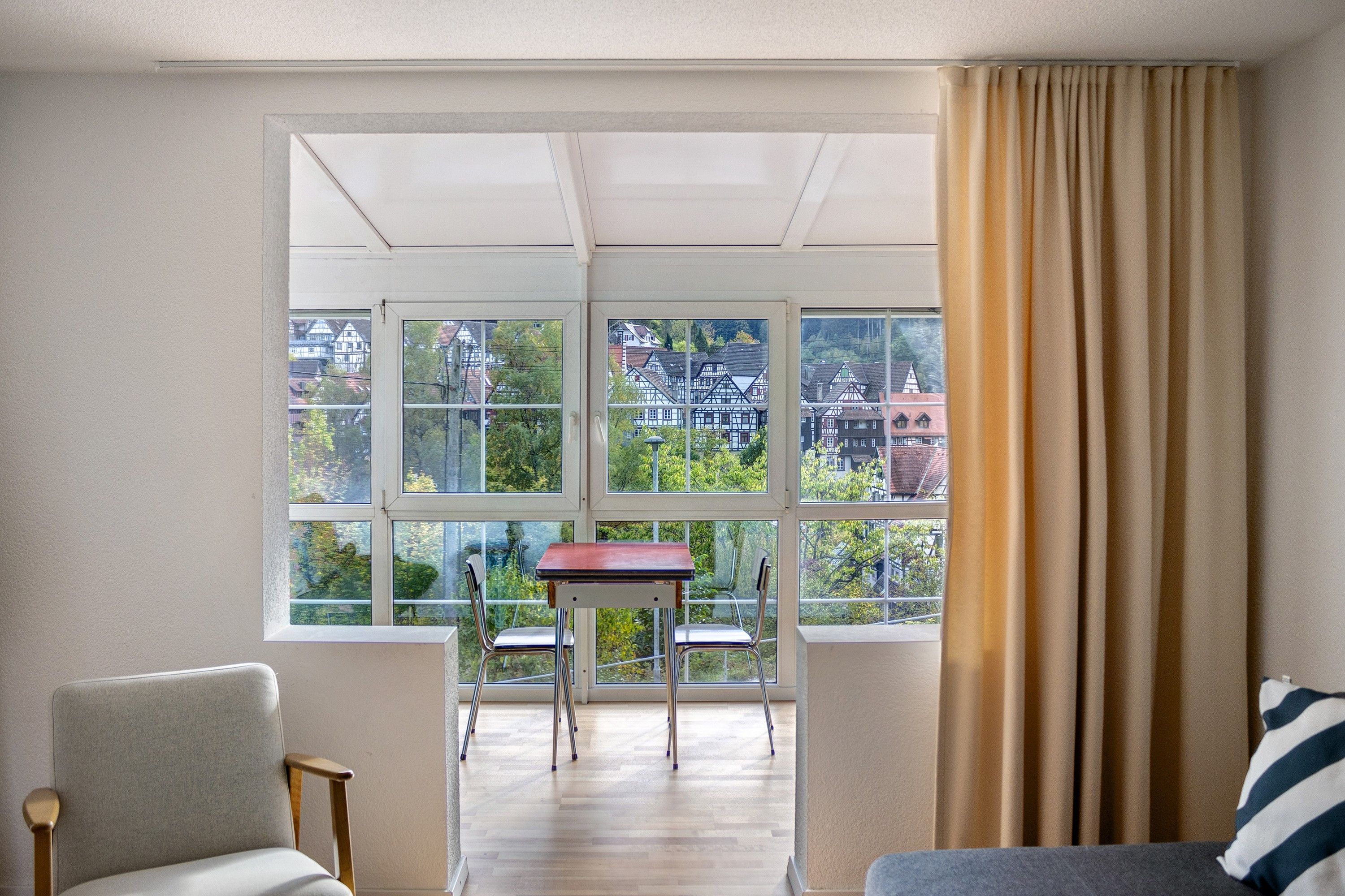 A room with a large window, a table, two chairs, and a sofa.