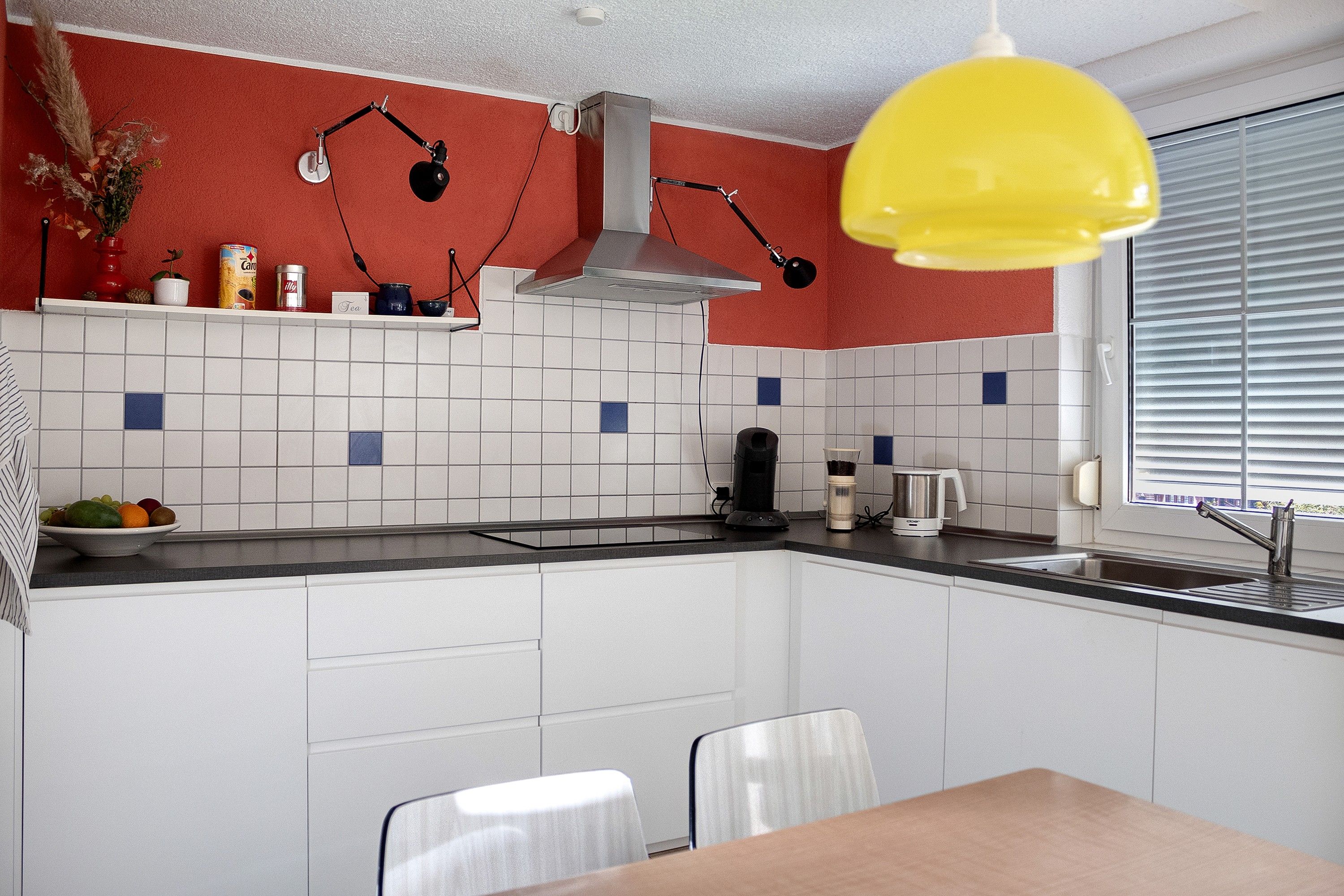 A kitchen with white cabinets, a black countertop, a yellow pendant light, and a window with blinds.