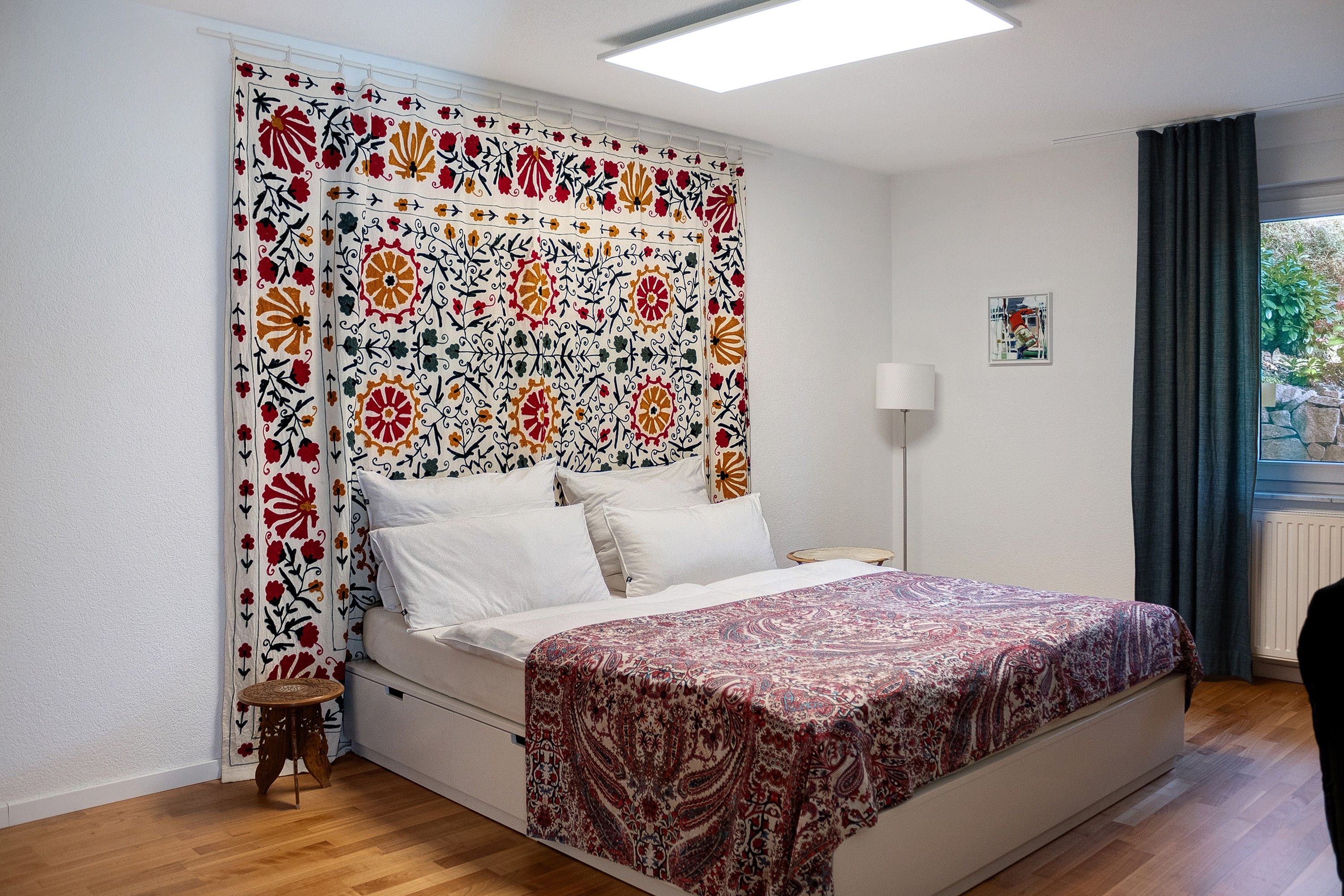 A bedroom with a bed, a bedside table, a lamp, and a window with curtains.