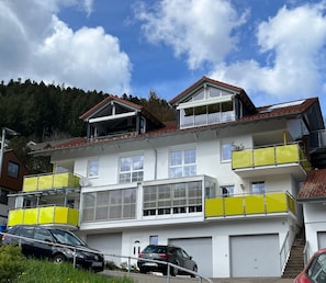 Ein mehrgeschossiges Wohngebäude mit weißer Fassade, mehreren Balkonen und einer Garage.