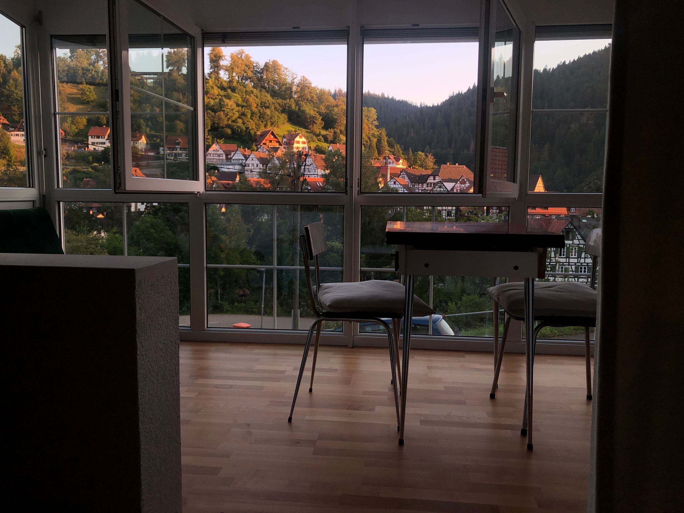 Una habitación con ventanas amplias, suelo de madera y dos sillas.