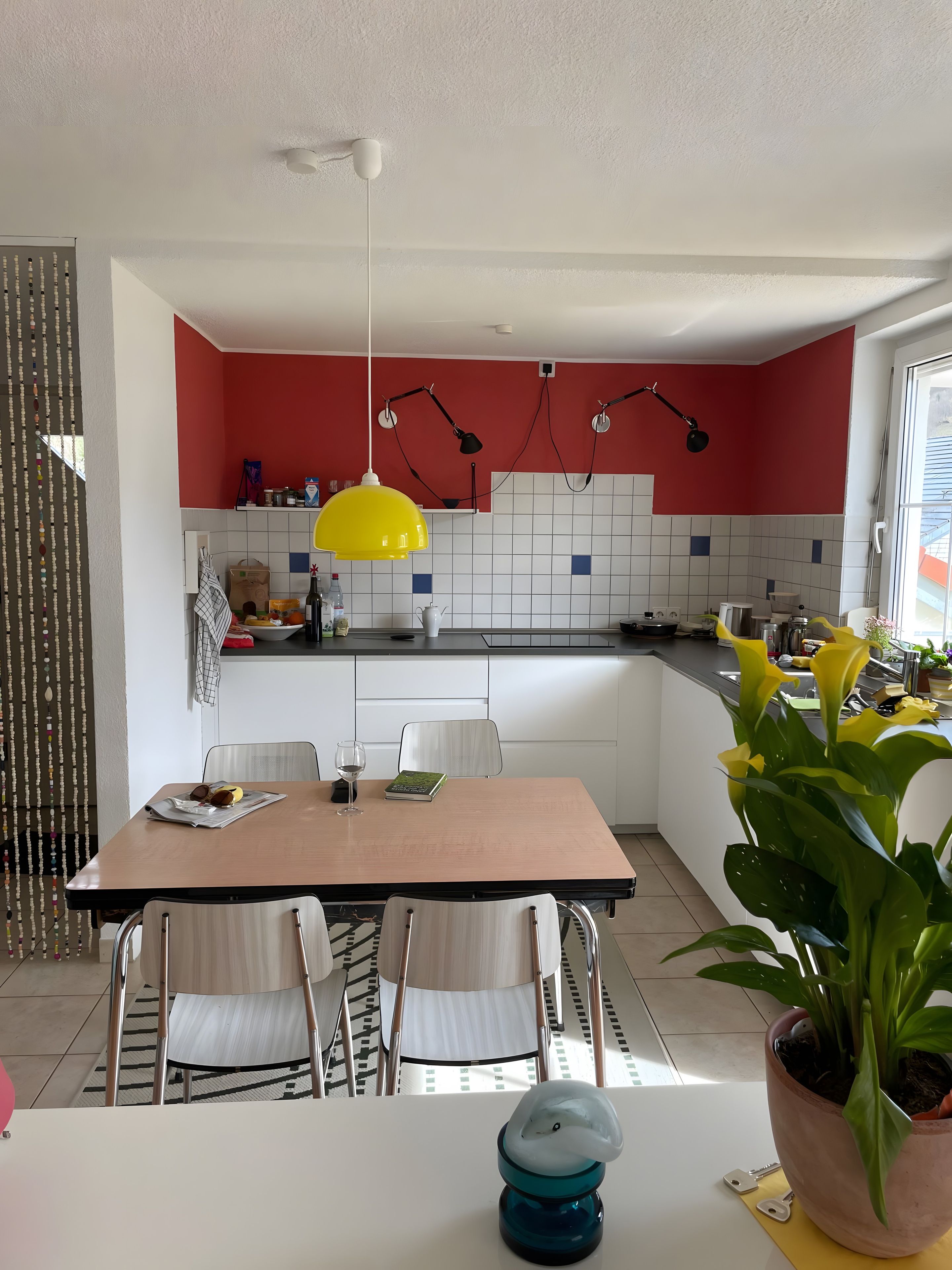 Eine moderne Küche mit weißen Schränken, einer roten Akzentwand und einer gelben Pendelleuchte.