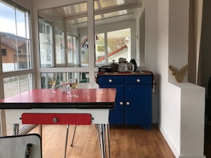 Ein Zimmer mit Tisch, Stühlen, einem blauen Schrank und großen Fenstern.