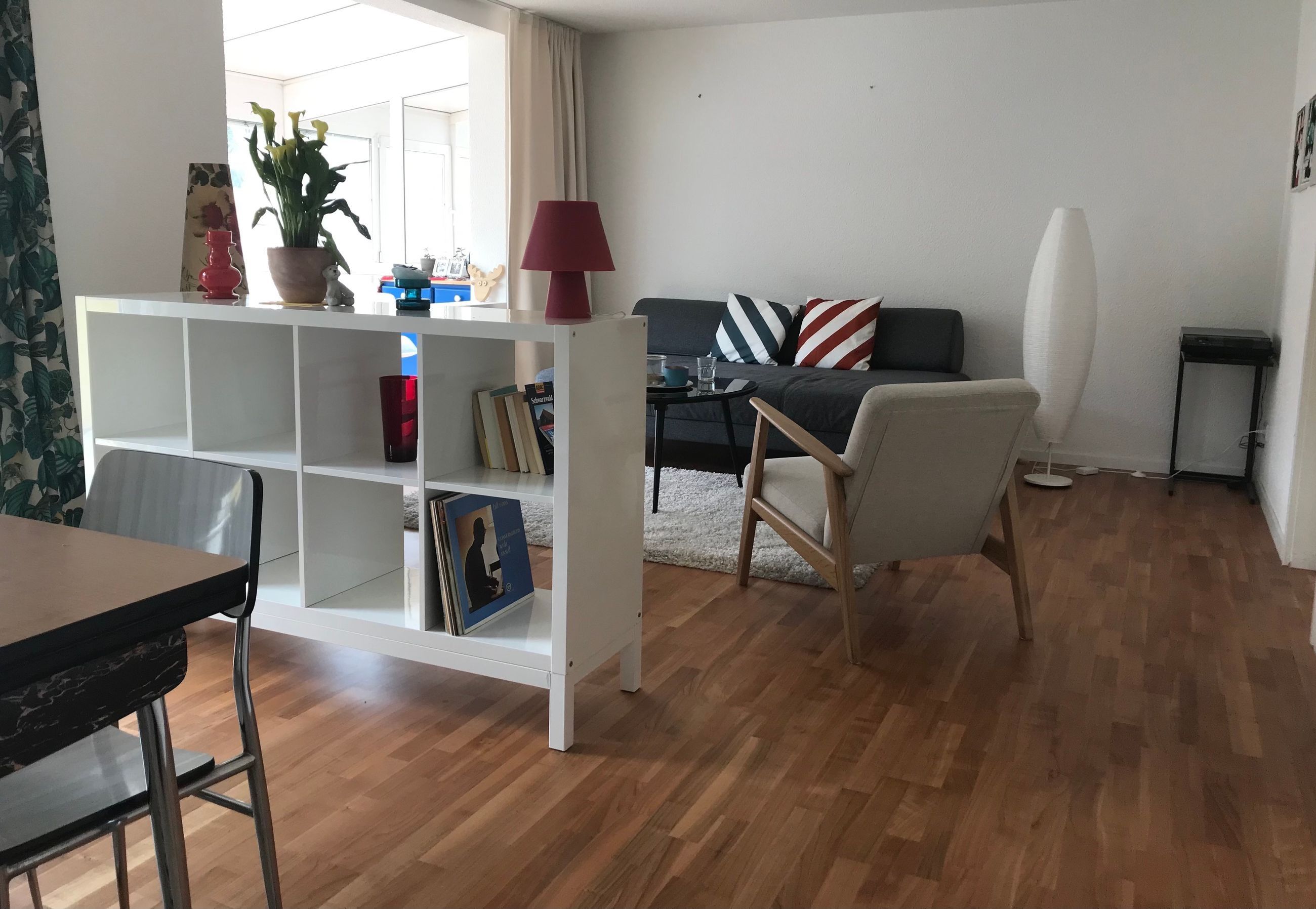 Una sala de estar con un sofá, una mesa de centro, una estantería, un sillón y una lámpara.