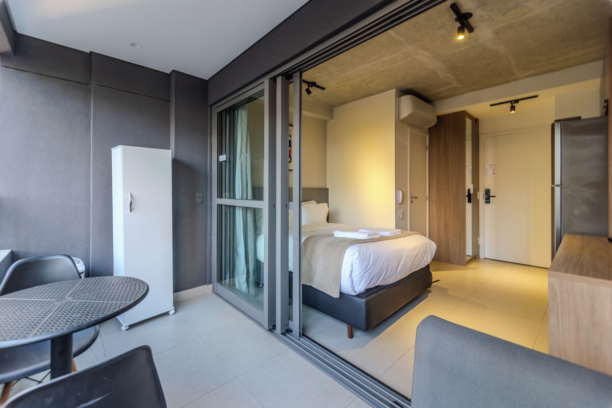 A modern hotel room with a bed, a small table, and a refrigerator.