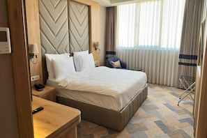 A hotel room with a large bed, a bedside table with a lamp, a chair, and a view of the outdoors through the window. - Vienna House by Wyndham Istanbul Bahcelievler (Istanbul)