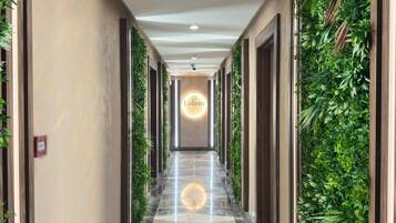 Un couloir doté d’un luminaire circulaire central, bordé de murs couverts de plantes grimpantes, qui mène à une porte sur laquelle est apposée une enseigne.