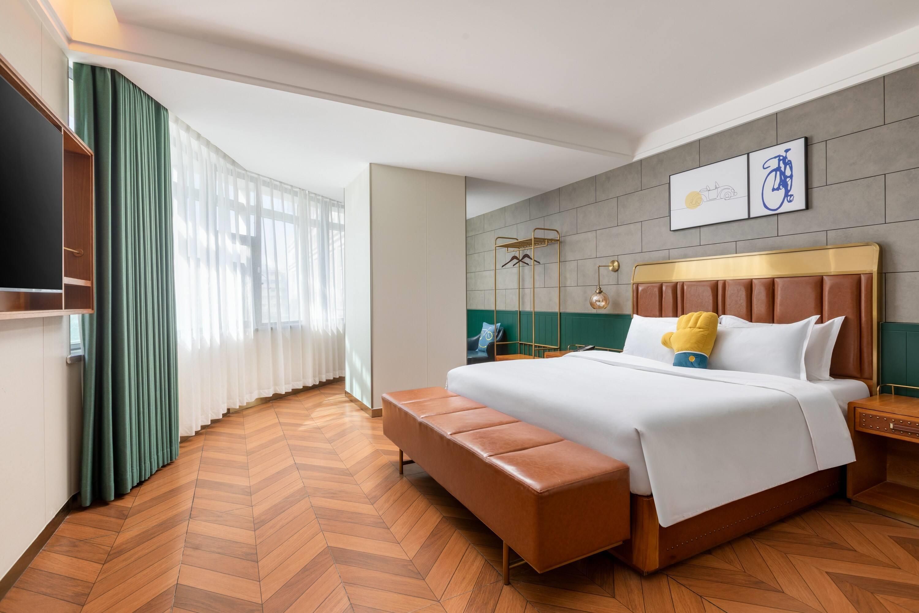 Quarto de hotel com uma cama grande, um banco, uma televisão e uma peça de arte de bicicleta na parede.