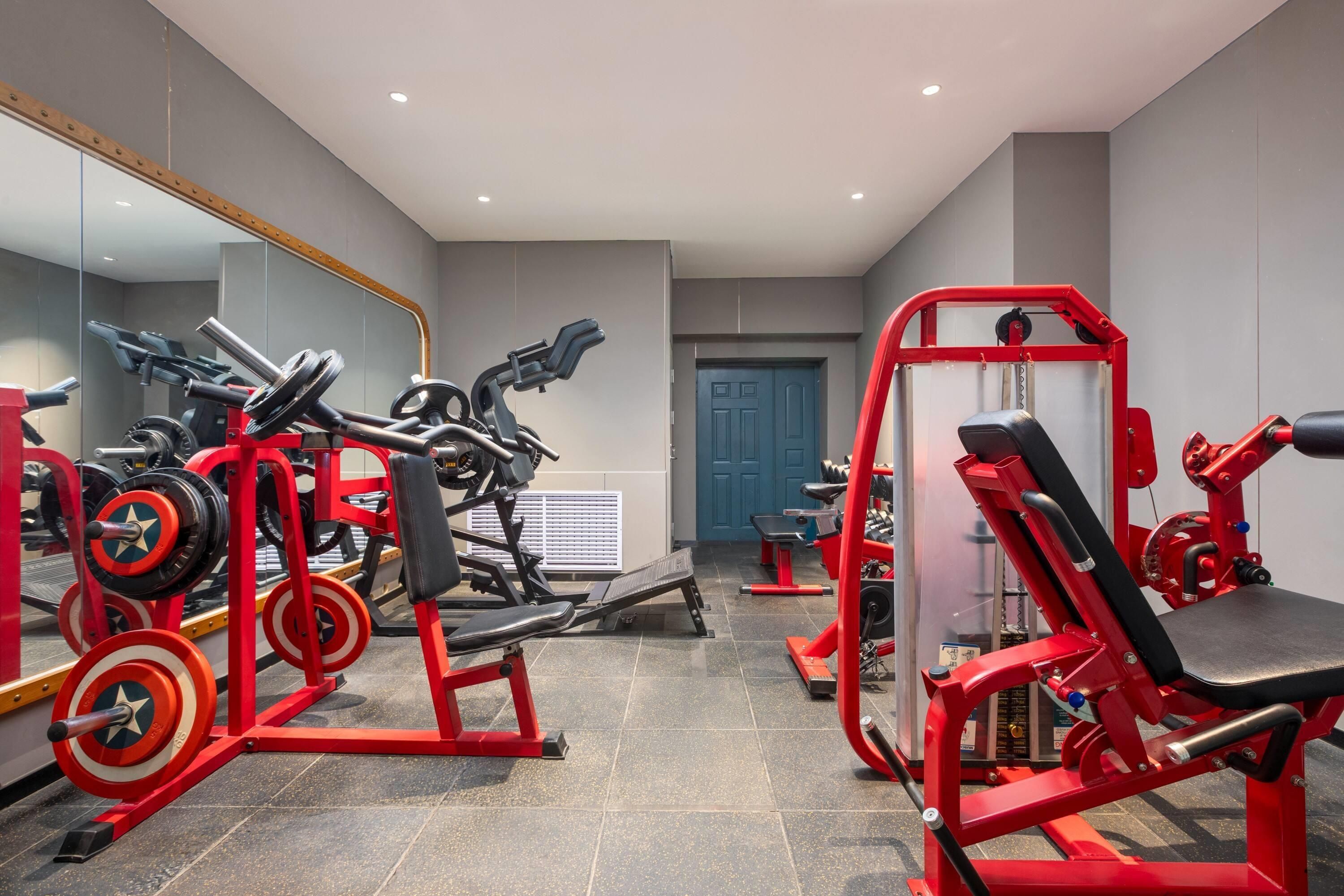 Een fitnessruimte met diverse trainingsapparaten, een grote spiegel en een deur.