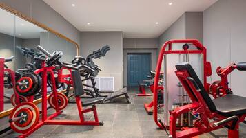 Een fitnessruimte met diverse trainingsapparaten, een grote spiegel en een deur.