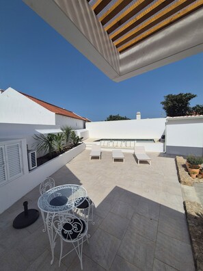 A rooftop patio with a table and chairs, a pool, and a white building with a red-tiled roof. - Vacation home in Ericeira for a short stay (Ericeira)