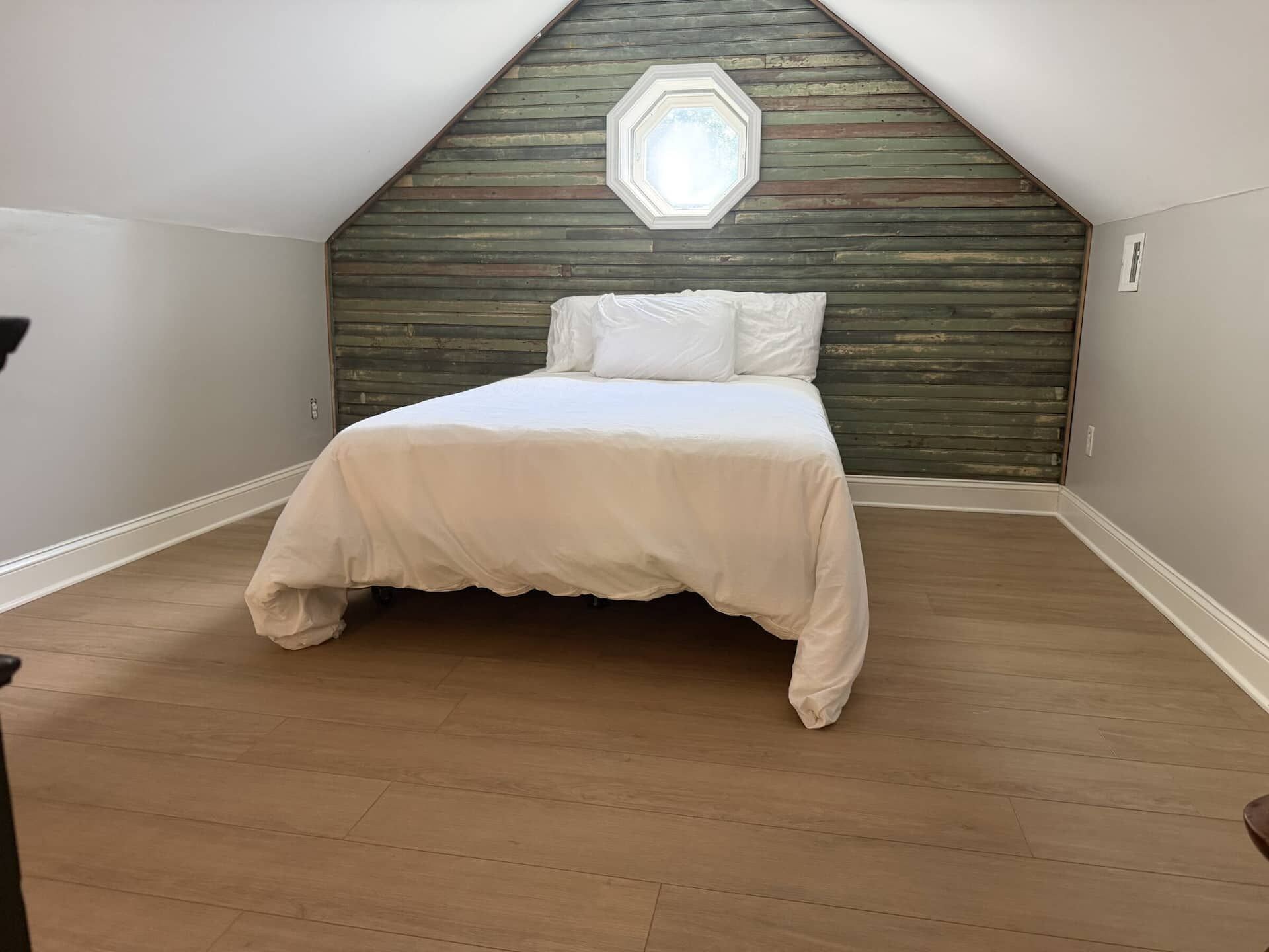 A bedroom with a sloped ceiling, a bed with white bedding, and a wooden headboard.