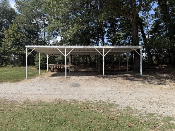 A covered outdoor area with a gravel ground, surrounded by trees.