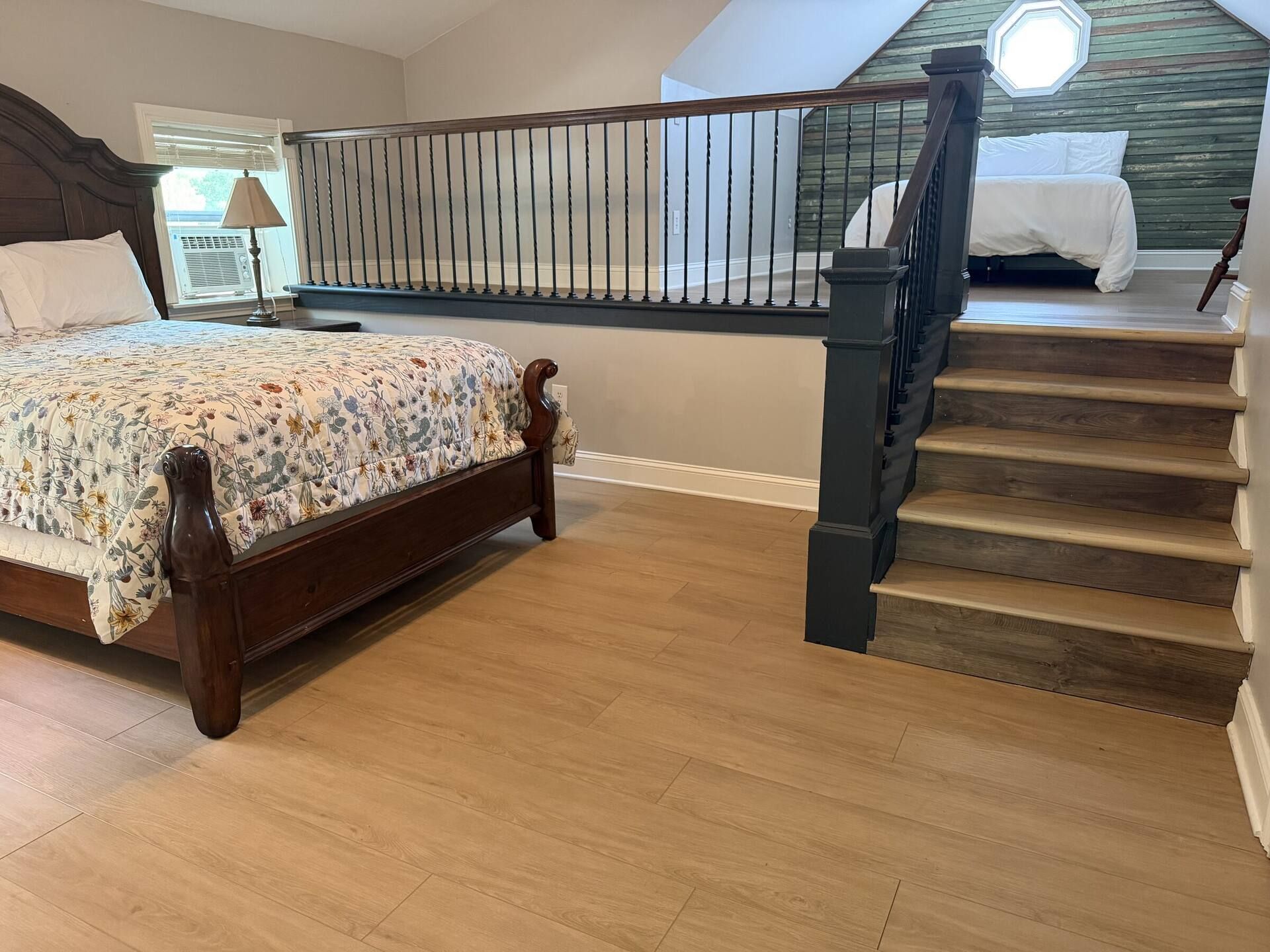 A bedroom with a wooden bed, a staircase, and a view of the outdoors.