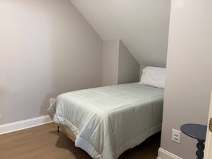 A bedroom with a single bed, a sloped ceiling, and a small bedside table.