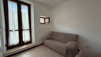 A room with a beige sofa, a small window with a mirror, and a tiled floor.