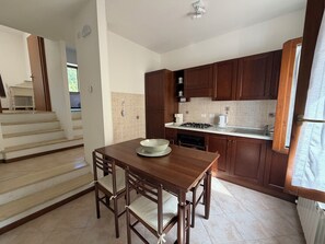 A kitchen with a dining table and chairs, a stove, cabinets, and a window. - Appartamento Collazzolo 4 by Ospitaci (Foligno)