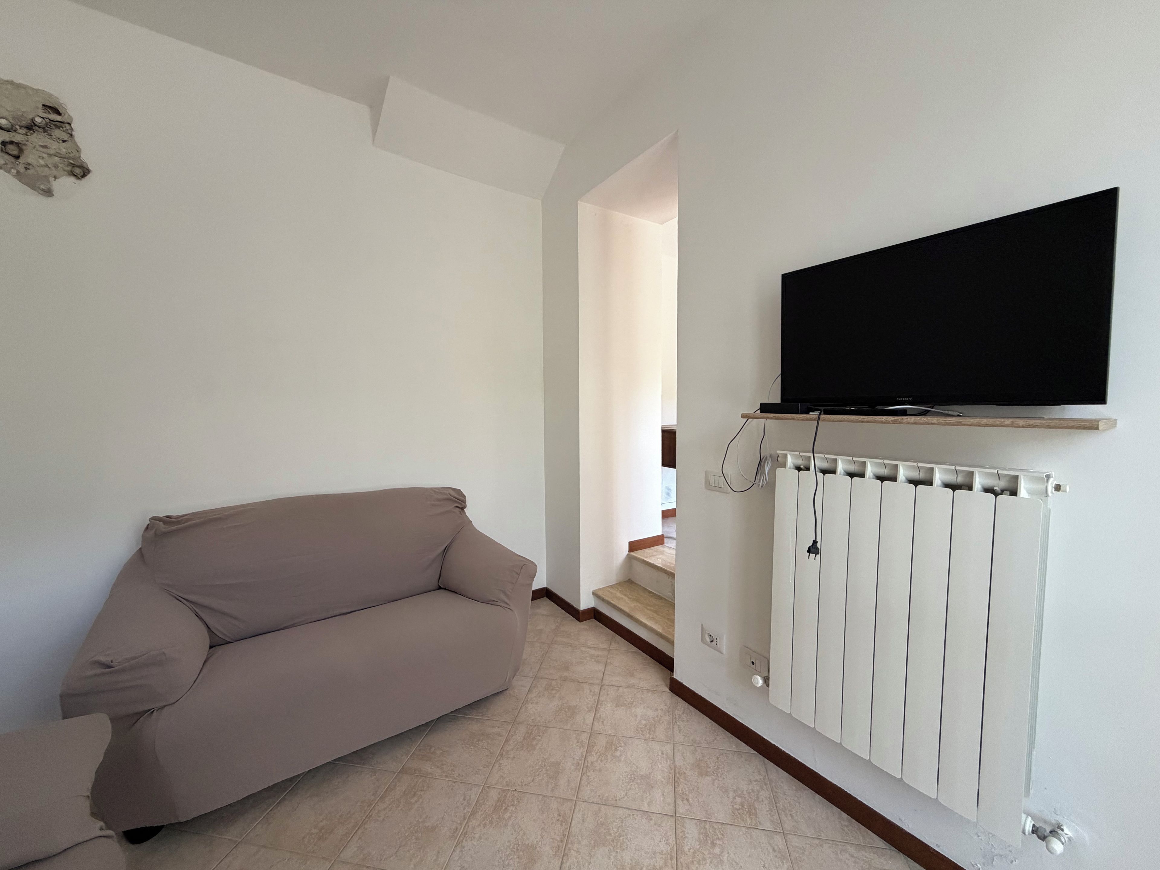 Ett vardagsrum med en beige soffa, en väggmonterad TV och ett vitt element.