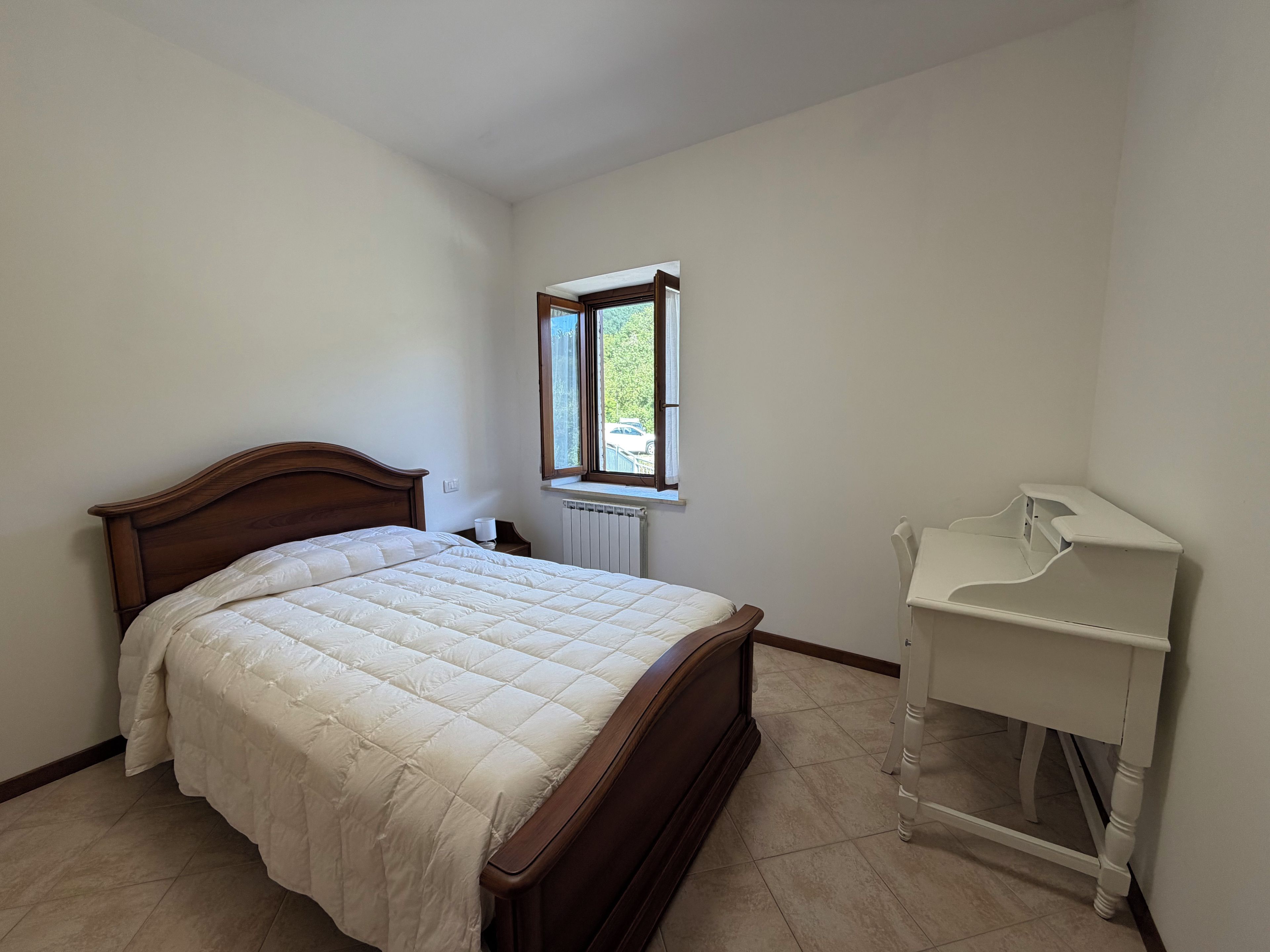 Una camera da letto con un letto di legno, un comodino bianco e una finestra vista verde.
