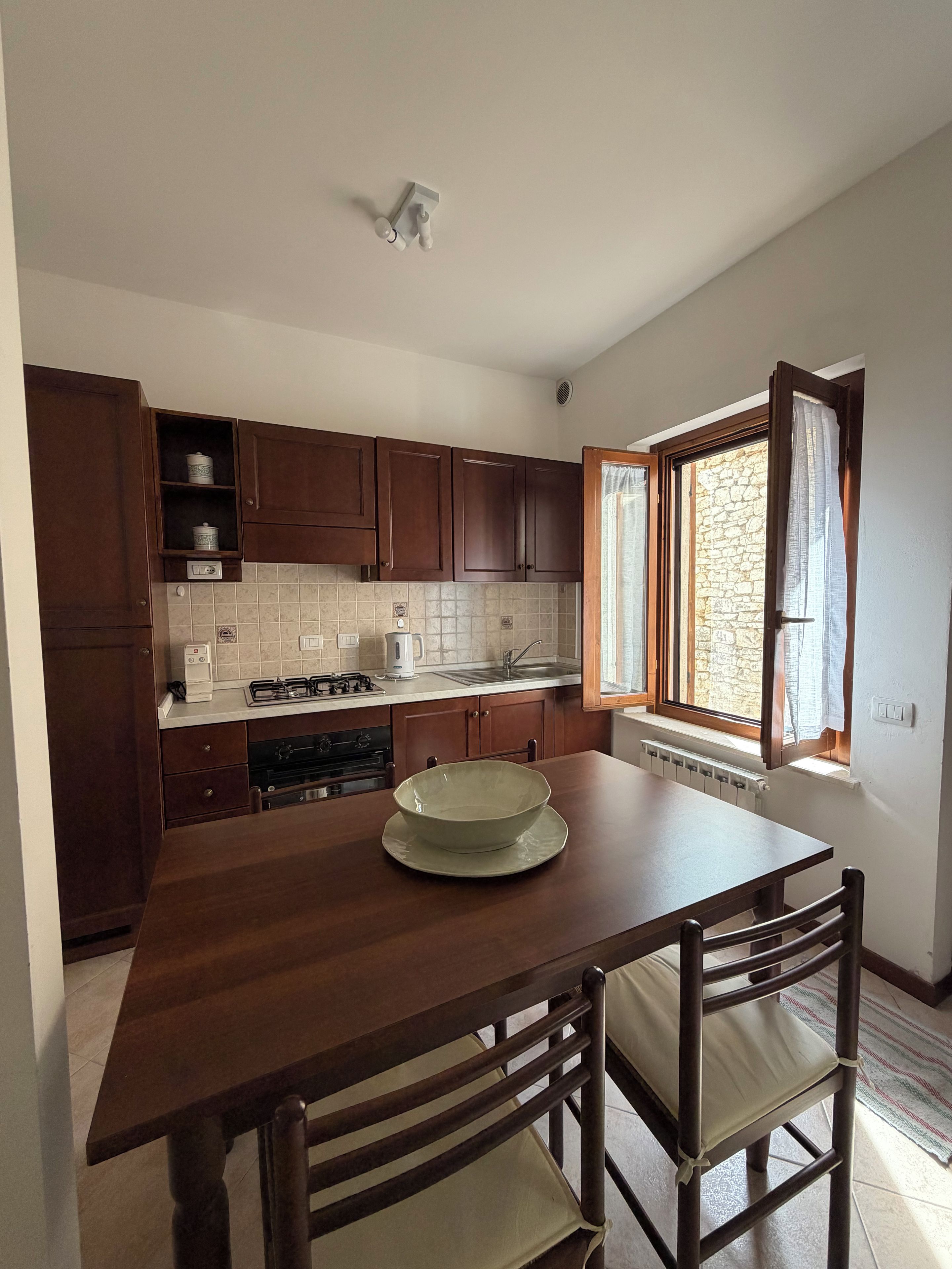 A kitchen with wooden cabinets, a stove, a sink, and a window with curtains.