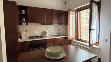 A kitchen with wooden cabinets, a stove, a sink, and a window with curtains.