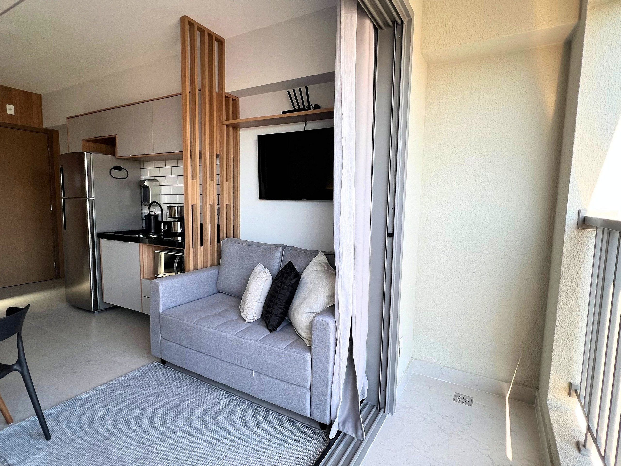 A compact living space with a kitchenette, a grey sofa, and a television.