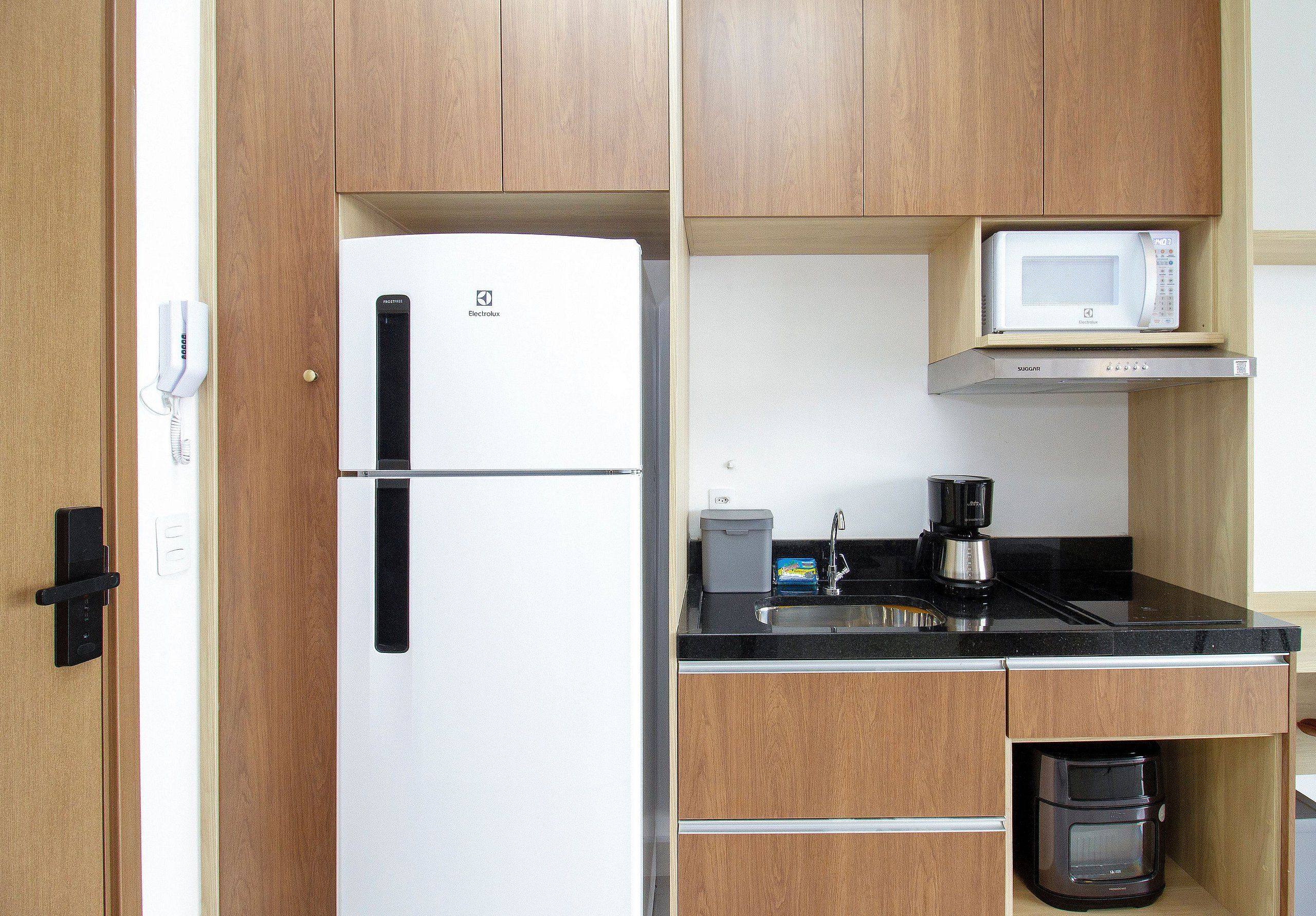 A compact kitchen with a white refrigerator, a microwave, a coffee maker, and a built-in oven.