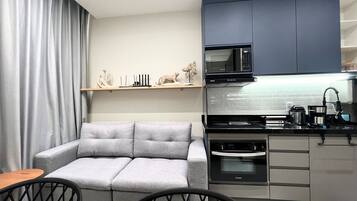 A compact kitchen with a grey sofa, a dining table with chairs, and a microwave above the stove.